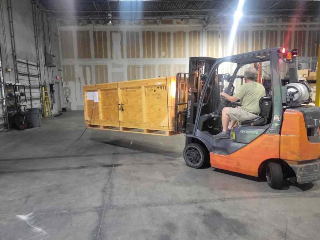Forklift operator repositioning large wooden crate for reload onto trailer